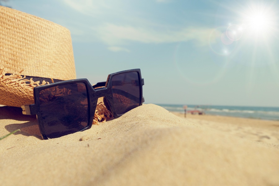 Beach Bag Essentials Close Up of Sunglasses Next to a Hat on a Beach