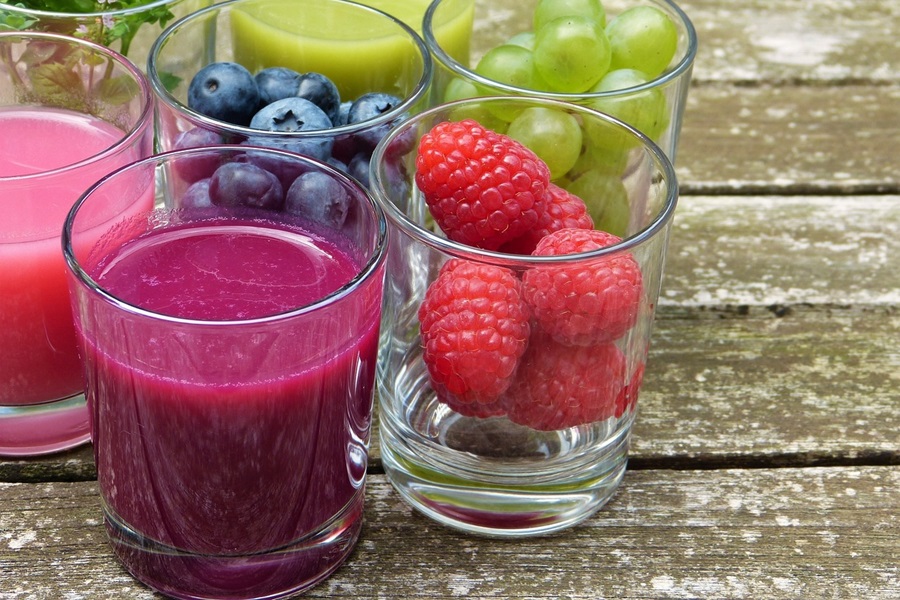 Smoothie Recipes to Reduce Bloating Close Up of a Smoothie Surrounded by Glasses Filled with Fruit,One Strawberries, One Grapes, and One Blueberries