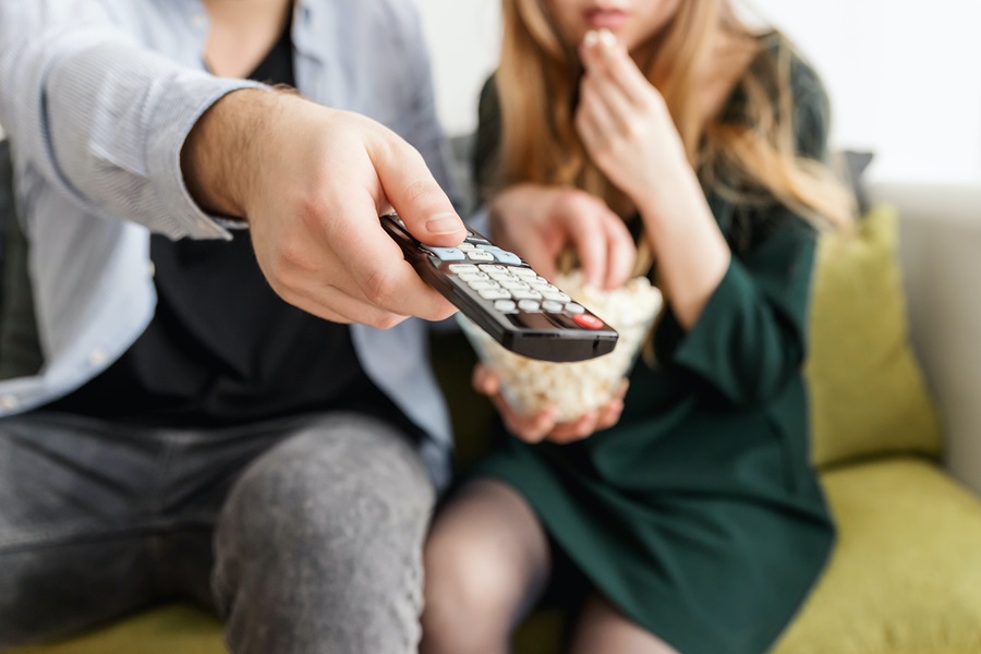 Amazon Fire TV Tips and Tricks Close Up of a Remote Control Being Pointed at a TV Being Held by a Man Sitting Next to a Woman Eating Popcorn