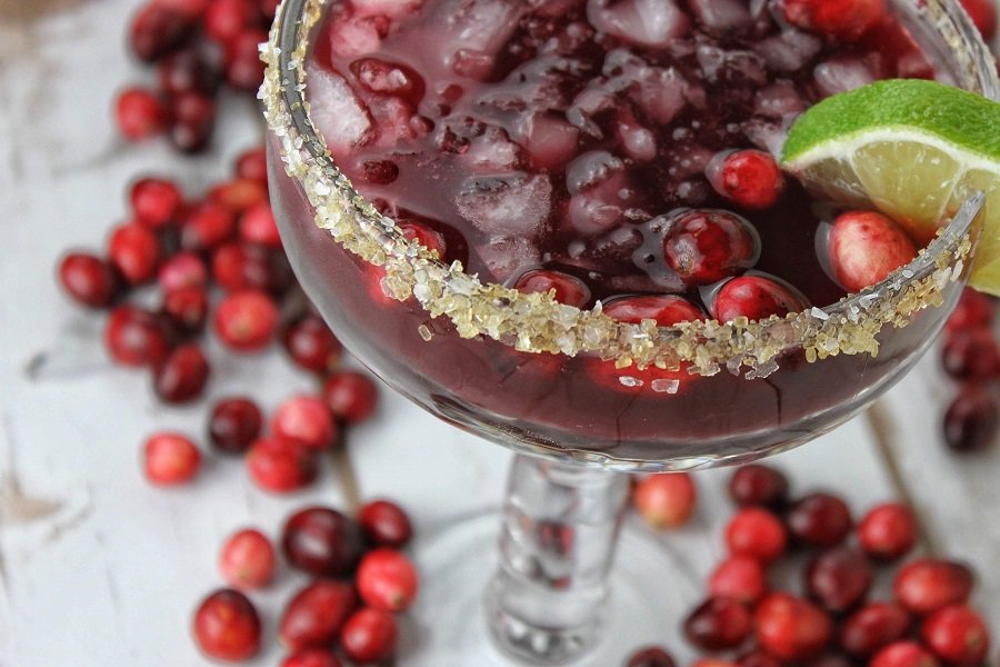 Winter Margarita Recipe Ideas Close Up of a Cranberry Margarita with Cranberries Scattered Around the Bottom of the Glass
