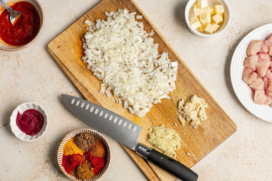Easy Chicken Tikka Masala Recipe with Coconut Milk Overhead View of Minced Onion, Garlic, and Ginger on a Cutting Board with a Knife