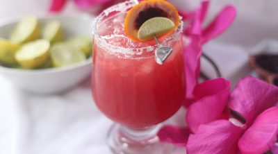 Blood Orange Margarita Recipe In a Glass Next to Flowers and a Small Dish with Lime Slices Inside