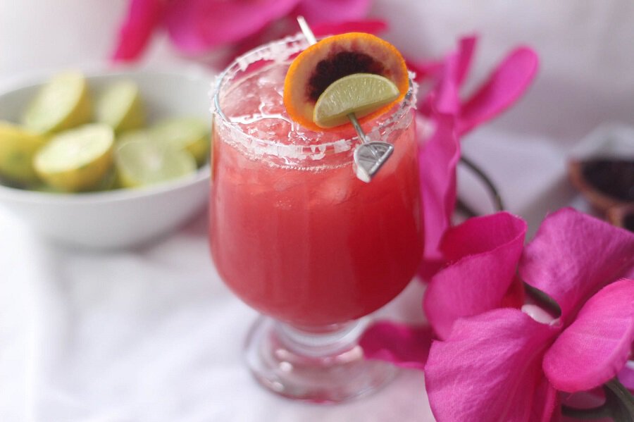 Blood Orange Margarita Recipe In a Glass Next to Flowers and a Small Dish with Lime Slices Inside