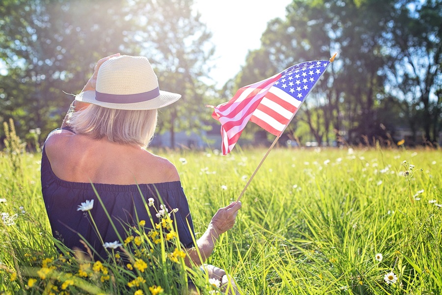 4th of July Party Ideas a Woman Wearing a Hat and Holding a Small American Flag Sitting in a Grassy Field