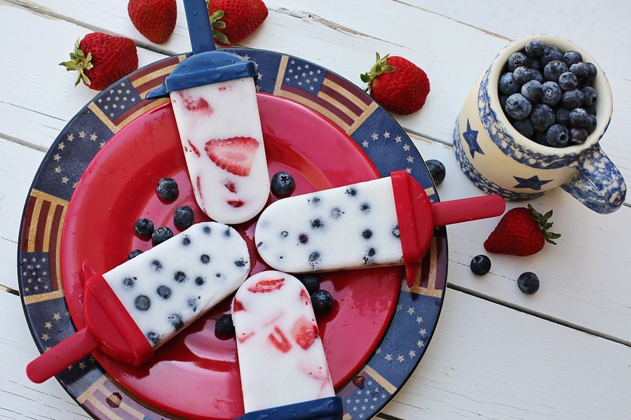 4th of July Party Ideas a Plate of White Popsicles Two With Strawberries and Two with Blueberries on an American Flag Plate