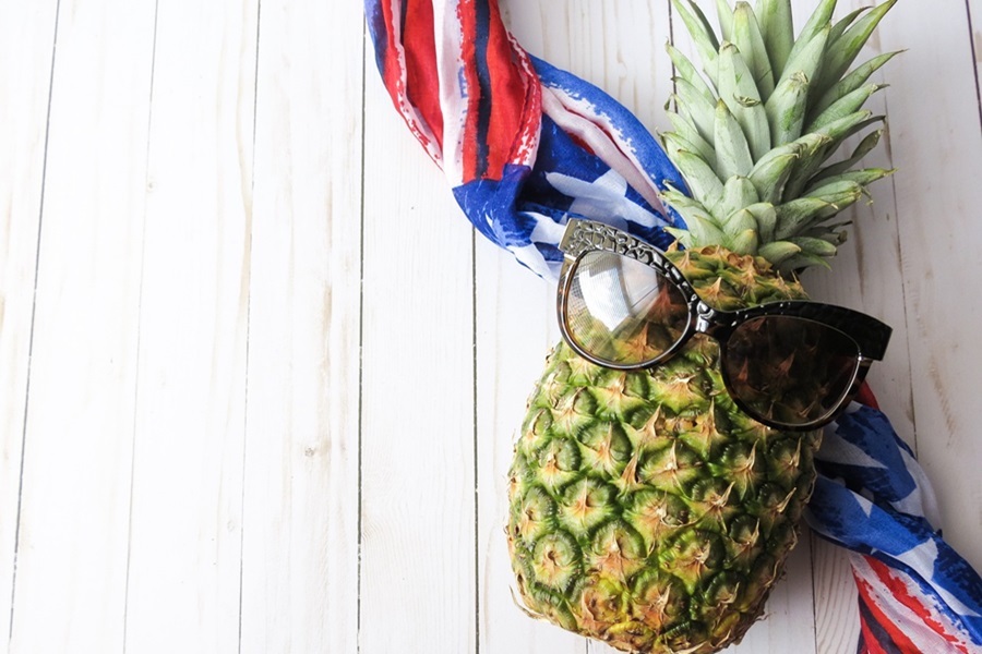 4th of July Party Ideas a Pineapple with Sunglasses On a Wooden Surface with a Red, White and Blue Scarf Behind it