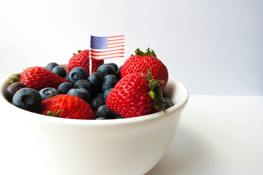 55 Patriotic Dessert Recipes Close Up of a White Bowl with Strawberries and Blueberries with a Small American Flag Toothpick