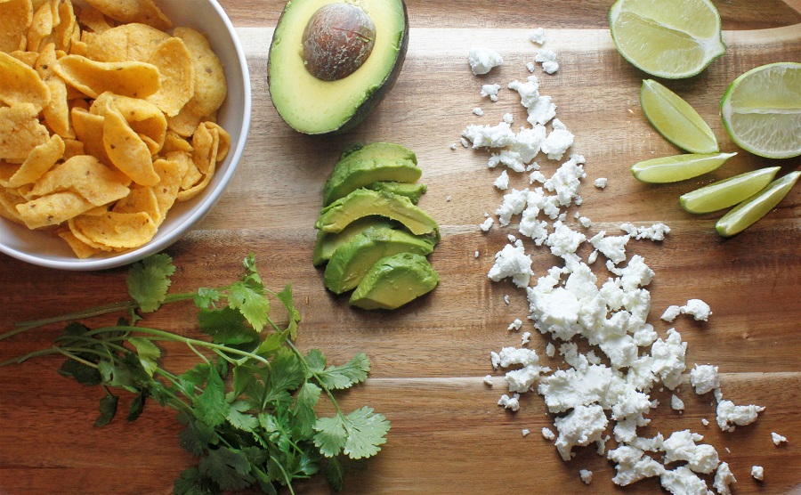 Low Carb CrockPot Recipes with Chicken a Cutting Board with Goat Cheese, Avocados, Cilantro, Lime Wedges, and a Small Bowl of Fritos