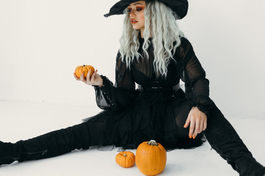 DIY Halloween Costumes For Adults a Woman Dressed as a Witch Sitting on The Floor Holding and Looking at a Small Pumpkin