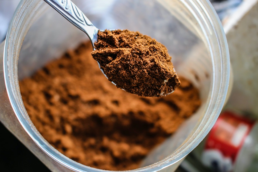 Best Protein Powder for Diabetics Close Up of a Spoonful of Protein Powder Hovering Above a Jar of Protein Powder
