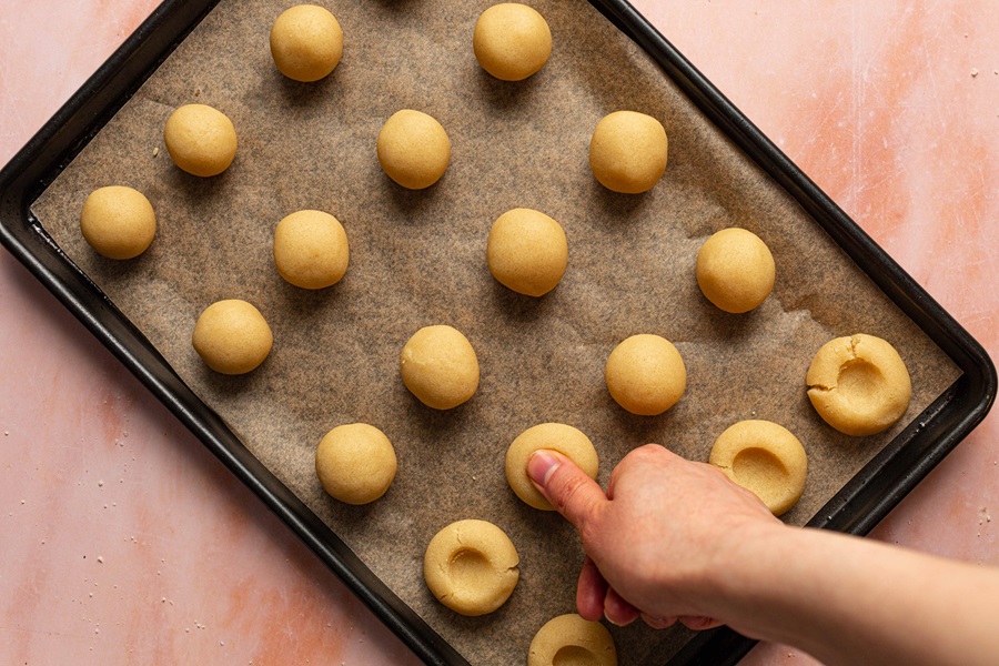 Thumbprint Cookies with Icing Recipe a Person's Hand Pushing a Small Indentation in Each Cookie on a Baking Sheet