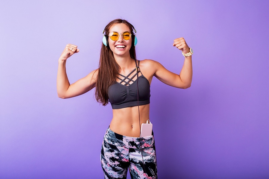 Is Core De Force on Beachbody OnDemand a Woman Wearing Workout Clothes Posing with Her Arms Flexing and a Purple Wall Behind Her