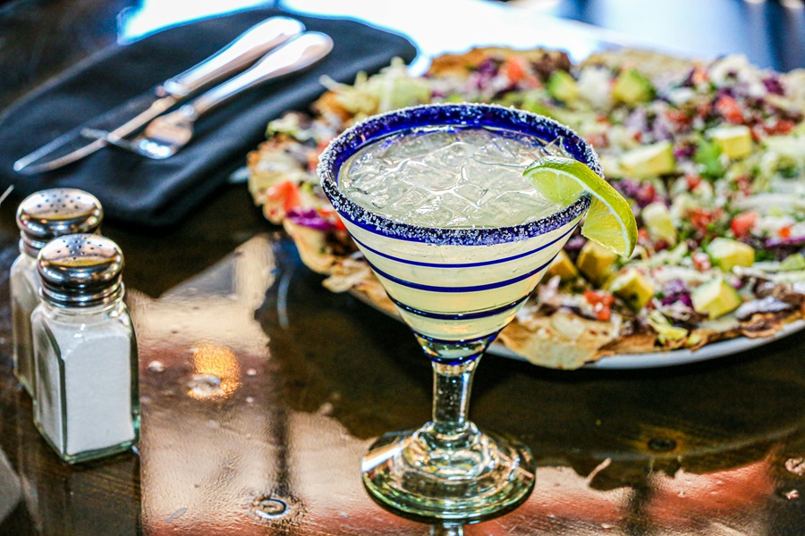 Limeade Margarita Recipe Ideas a Margarita in a Blue and Clear Glass Garnished with a Lime Slice Next to a Plate of Nachos
