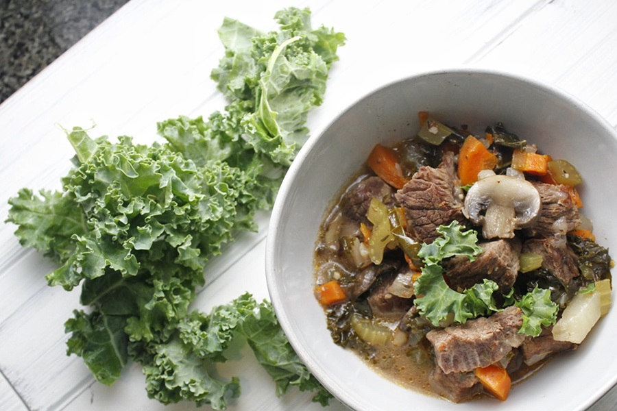 Slow Cooker Low Carb Beef Stew Recipe Overhead View of a Bowl of Stew with Kale Nearby on a Wooden Surface
