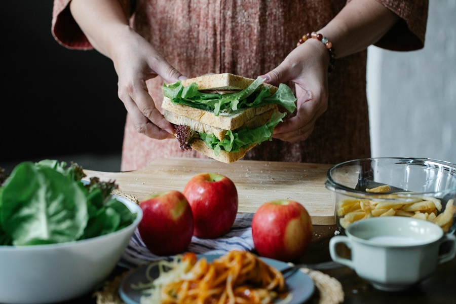 Is Gluten Free Bread Good for Diabetics Close Up of a Woman Holding a Sandwich with Apples, Lettuce and Other Ingredients on a Table in Front of Her