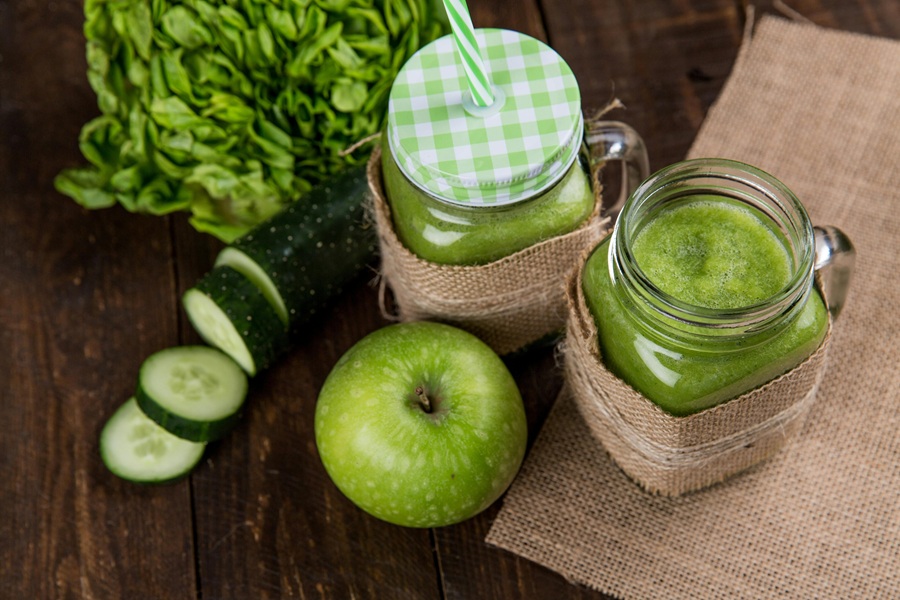 Fat Burning Juice Recipes  Overhead View of Two Small Mason Jars Filled with Green Juice Next to a Sliced Cucumber and Herbs