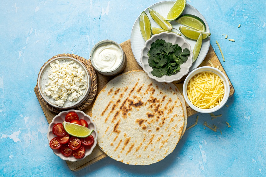 Ingredients for Easy Chicken Tacos with Shredded Chicken Separated into Small Bowls on a Blue Surface