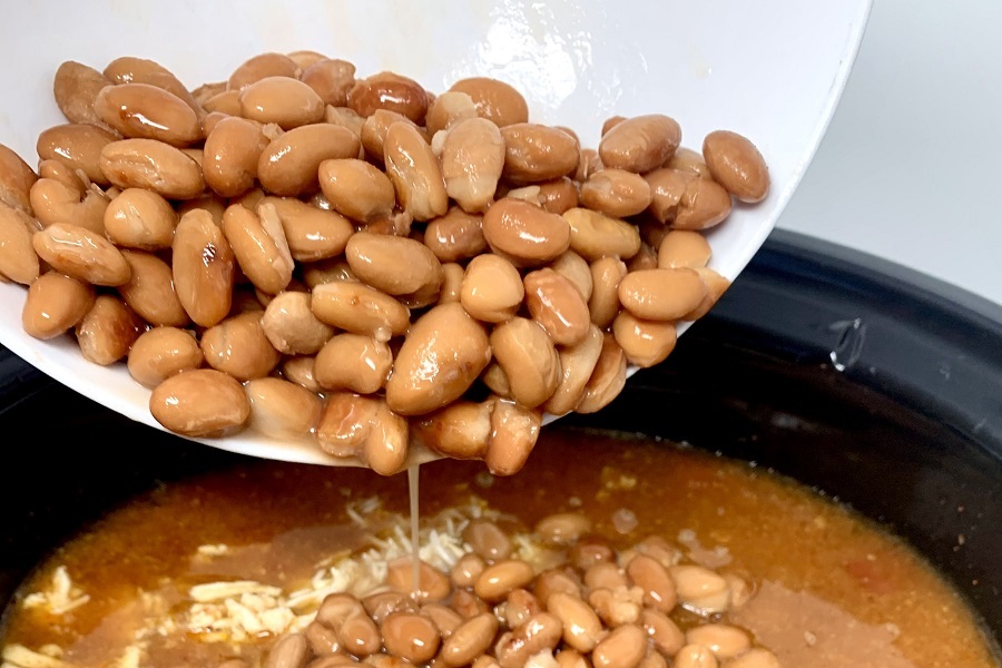 Easy Chicken Burrito Bowl Recipe Pinto Beans Being Poured Into a Crockpot Filled with Other Ingredients