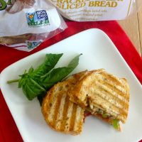 Pizza Sandwich Recipe Close Up of a Sandwich Cut in Half on a White Plate with a Sprig of Basil