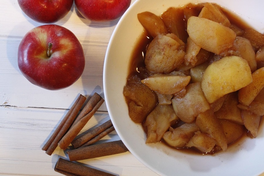 Faster Than Stovetop Instant Pot Cinnamon Apples Recipe in a Bowl Next to Cinnamon Sticks and Raw Apples