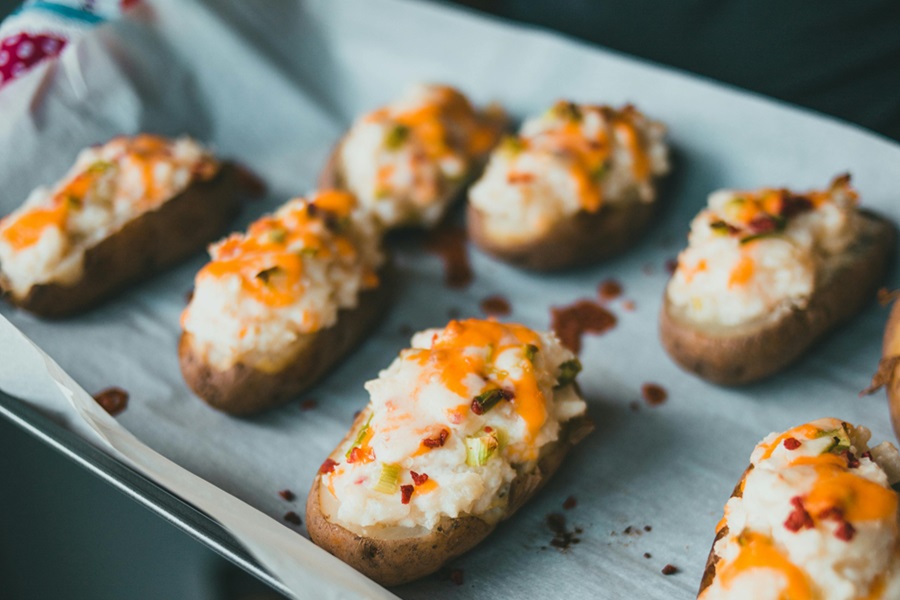 Baked Potatoes in the Oven a Baking Sheet Lined with Parchment Paper and Baked Potatoes Cut in Half with Cheese and Bacon