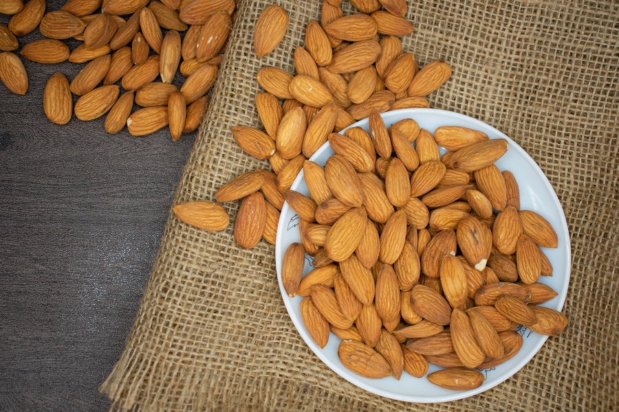 High Protein Grocery List Overhead View of a Plate of Almonds with Almonds Spilling Off onto a Brown Cloth