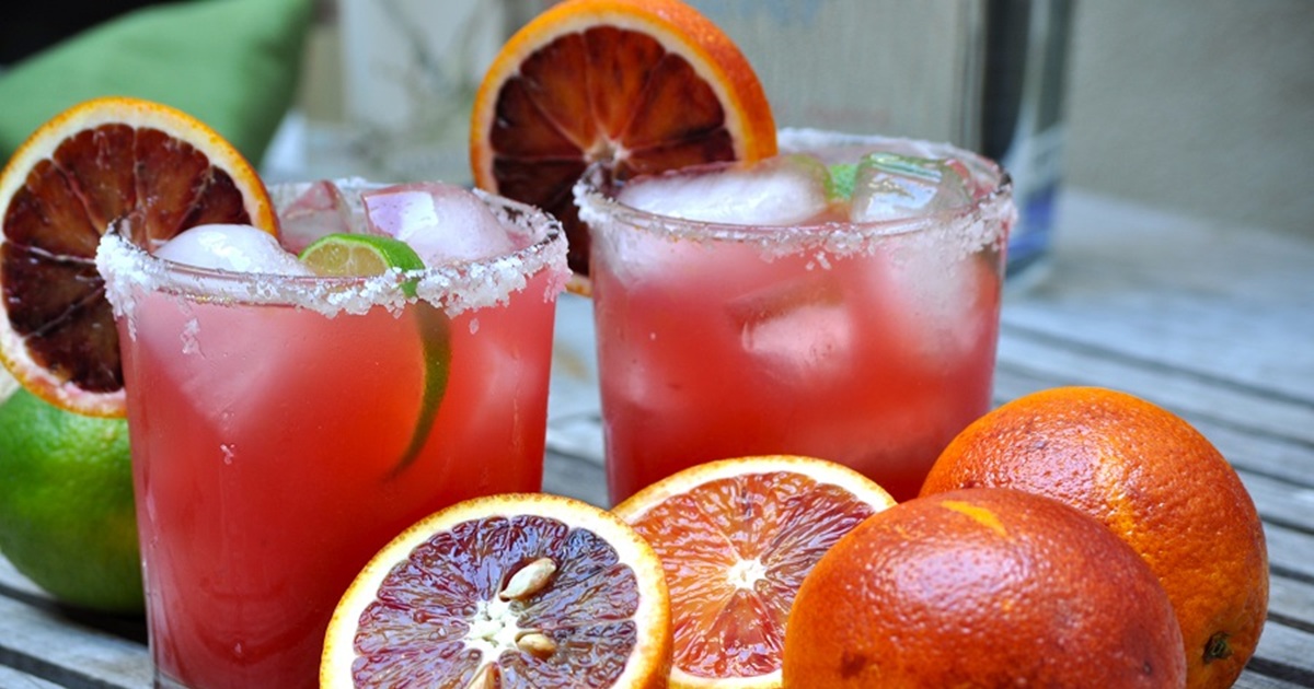 National Margarita Day Recipes Close Up of Blood Oranges with Two Blood Orange Sparkling Margaritas in the Background Garnished with Blood Orange Slices and Lime Slices