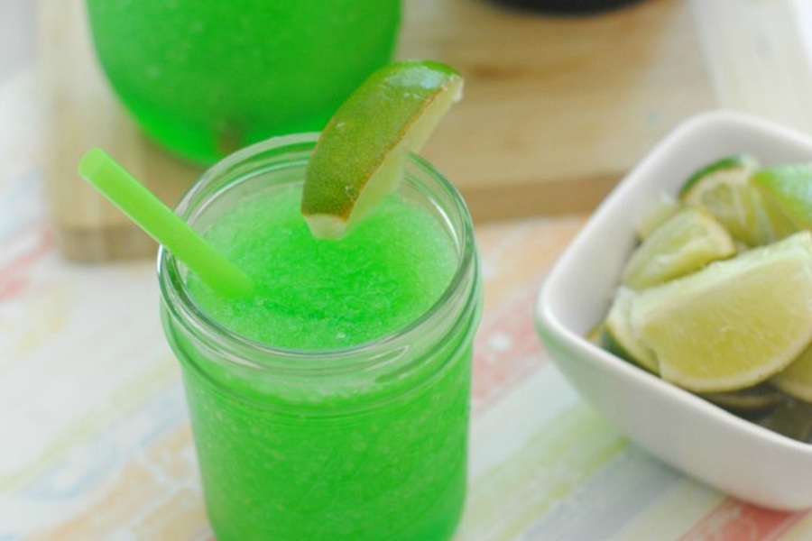 Green Drinks For Kids and Adults Frozen Kool-Aid Slushie in a Glass with a straw and a Lime Wedge