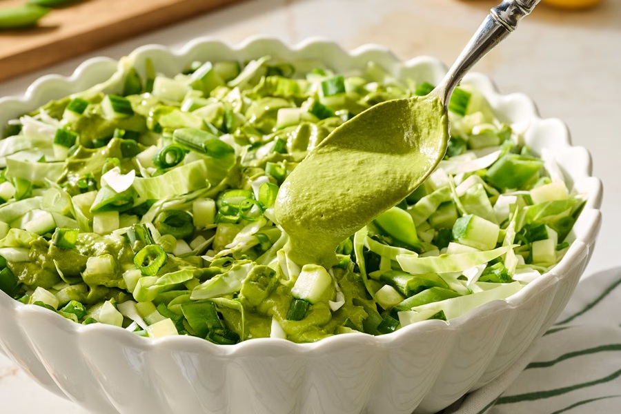 Healthy Easter Dinner Side Dishes Green Goddess Salad in a Bowl with a Spoon of Green Dressing Being Poured On Top