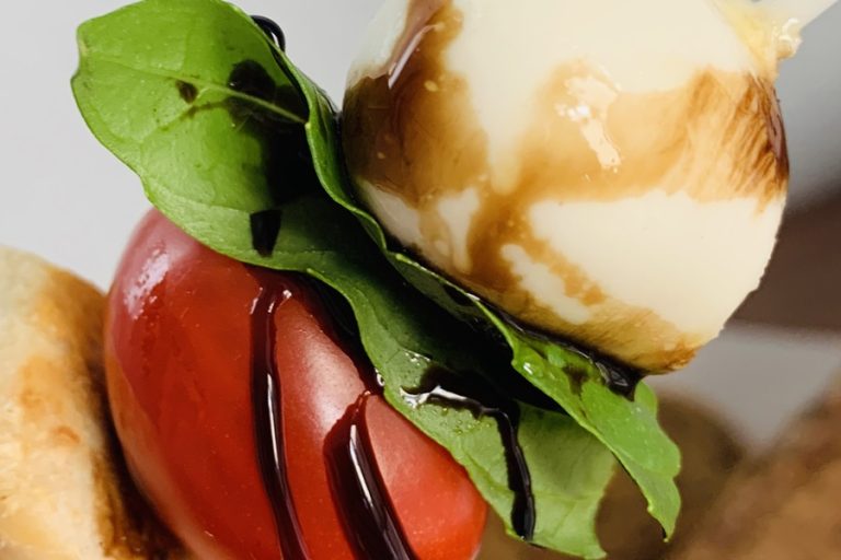 Dinner Ideas for Mother's Day Close Up of a Roma Tomato, Basil Leaf, and Mozzarella Cheese Stacked Together Drizzled with Balsamic Vinaigrette