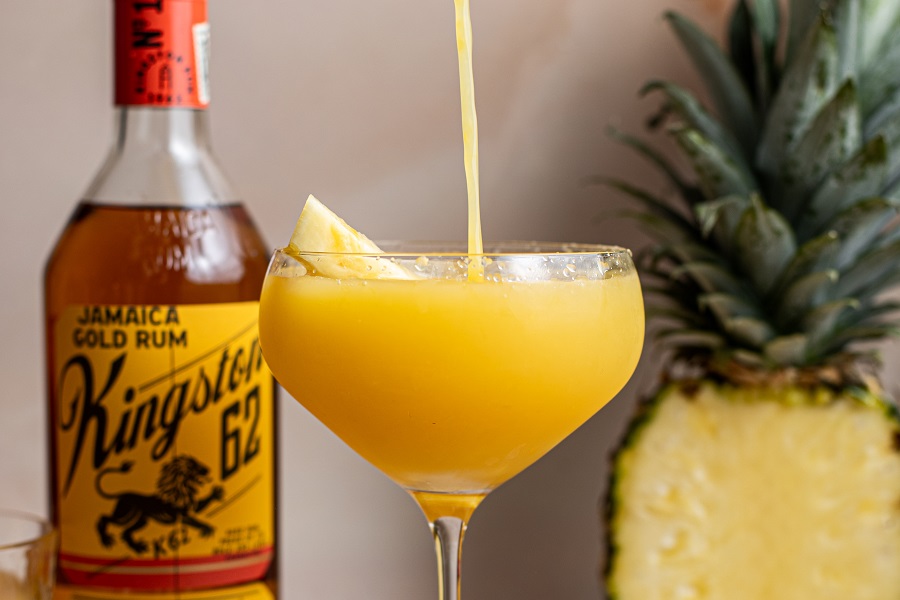 Best Boating Drinks Yellow Bird Rum Cocktail Being Poured into a Cocktail Glass with a Half a Pineapple in the Background