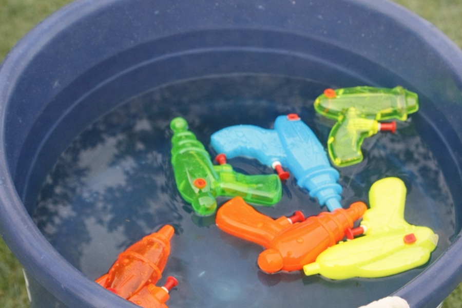 4th of July Party Ideas Neon-Colored Squirt Guns Floating in a Pool of Water Inside a Blue Bucket