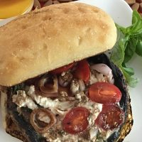 Portobello Mushroom Burger Topped with Cherry Tomatoes and Cheese on a White Plate