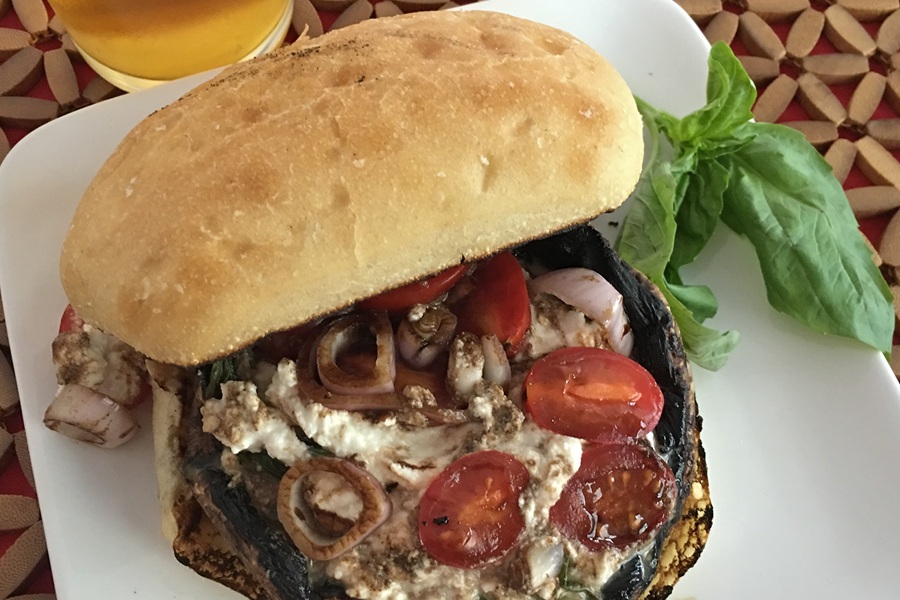 Portobello Mushroom Burger Topped with Cherry Tomatoes and Cheese on a White Plate