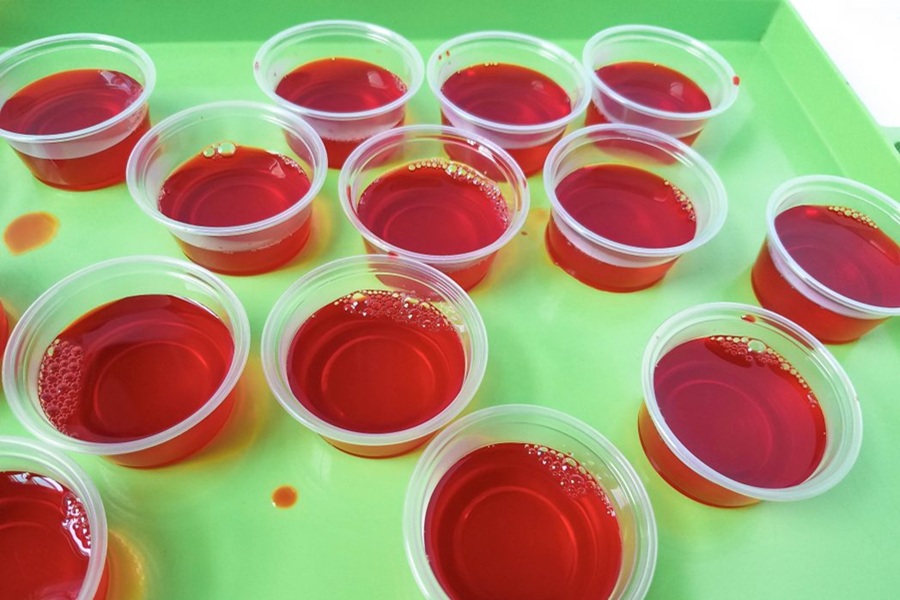 Easy Margarita Jello Shots Raspberry Jello Shots in Plastic Cups on a Green Tray