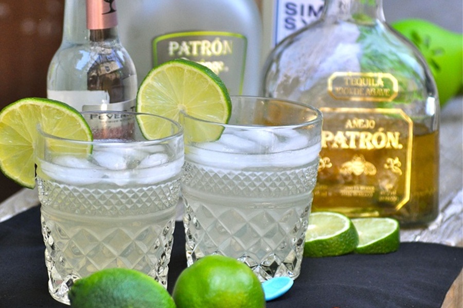 Low Carb Margarita Recipe Close Up of Two Margaritas Garnished with Lime Slices and Bottles of Patron in the Background