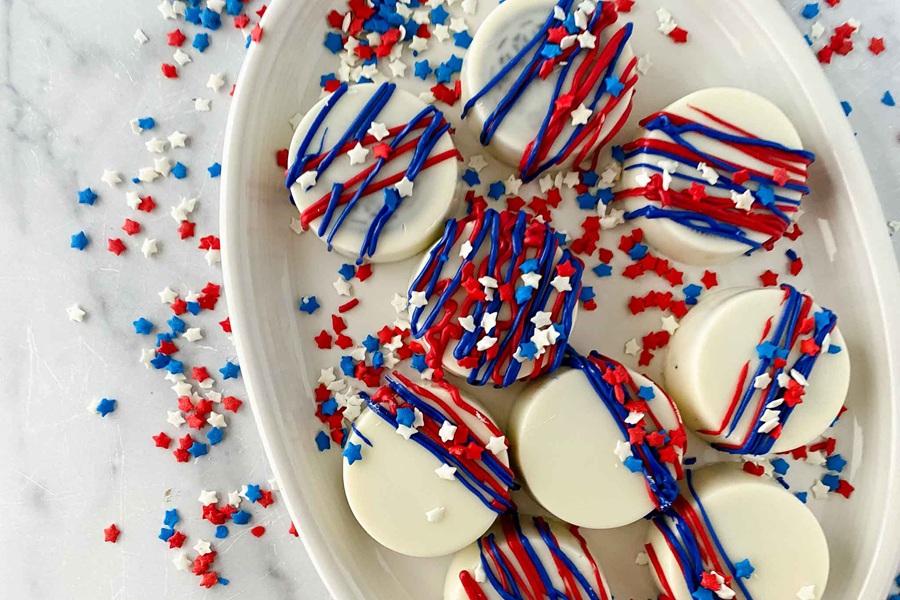 Patriotic Dessert Recipes Easy July 4th Themed Chocolate Covered Oreos on a White Plate with Red, White and Blue Sprinkles