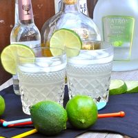 Low Carb Margarita Recipe Two Margaritas in Glasses Garnished with Lime Slices Two Limes in Front and Bottles of Alcohol in the Background
