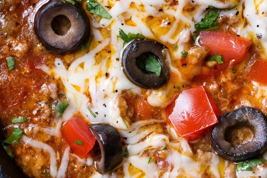 Crockpot Halloween Recipes Close Up of Taco Dip Topped with Black Olives, Diced Tomatoes, and Cheese