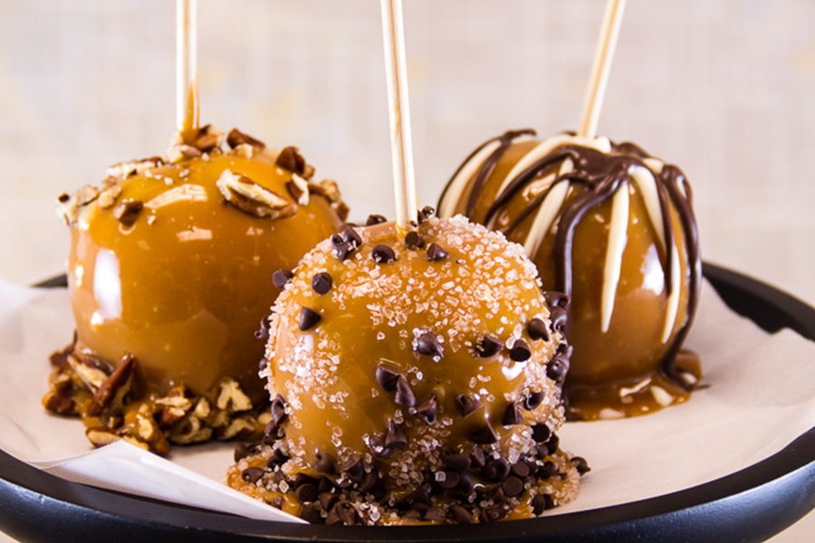 Crockpot Halloween Recipes Three Caramel Apples Topped with Chocolate Chips, Syrup, and White Sprinkles