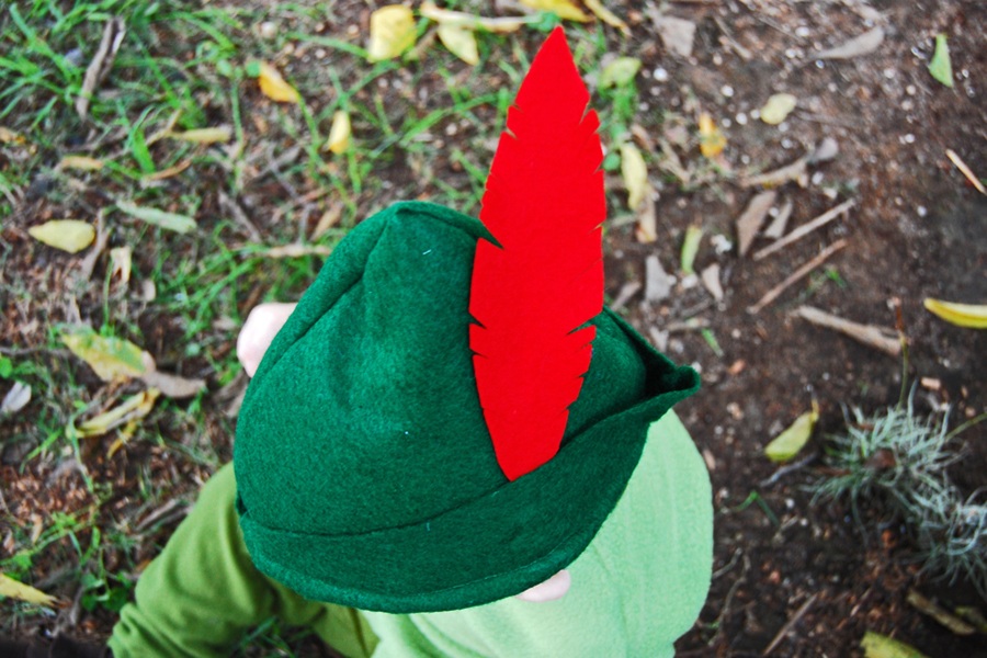 DIY Halloween Costumes For Kids a Little Boy Wearing a Peter Pan Hat Sitting on the Ground Outside