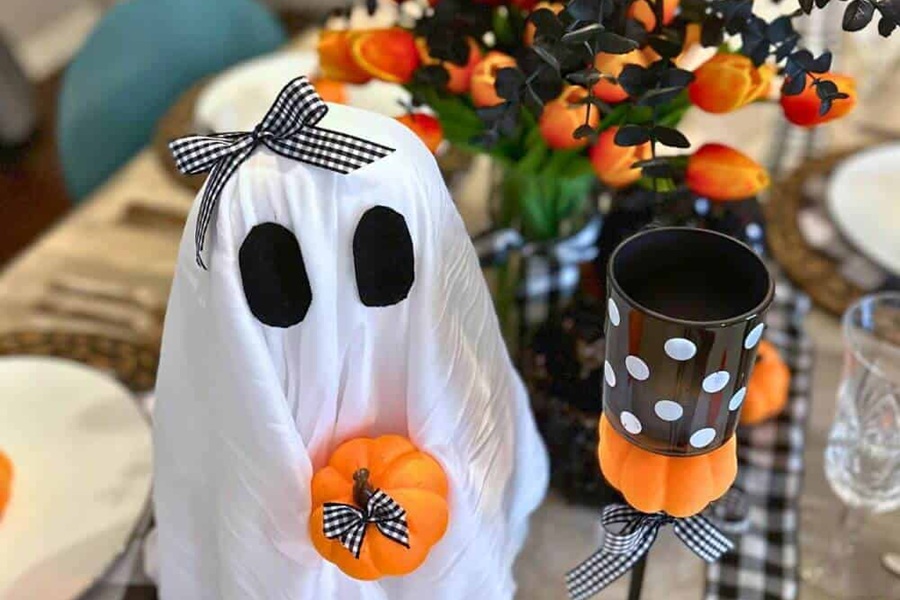 DIY Halloween Decorations a Small Ghost Holding a Smaller Pumpkin Next to a Black, White, and Orange Centerpiece on a Table