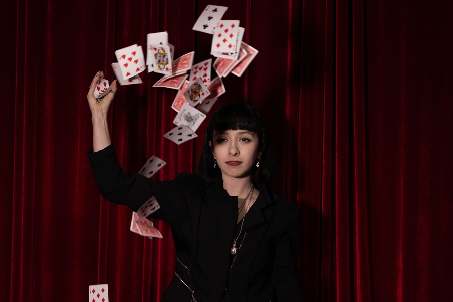 Downloads for your Halloween Playlist a Woman Wearing a Magicians Top Hat with Her Arm Up in the Air and Playing Cards Scattered Around in the Air Around Her
