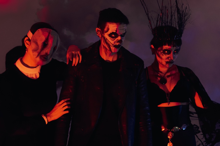 Downloads for your Halloween Playlist Three People with Monster Makeup on Their Faces Standing in a Dark Room with a Red Glow on Their Faces