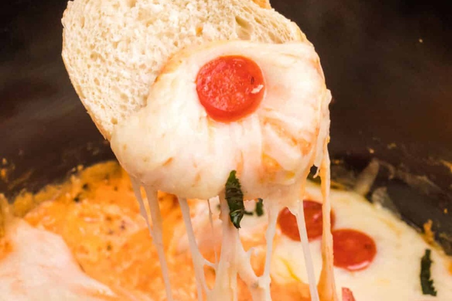 Spooky Halloween Crockpot Recipes a {iece of Bread Being Dipped into Pizza Dip with Cheese and Pepperonis